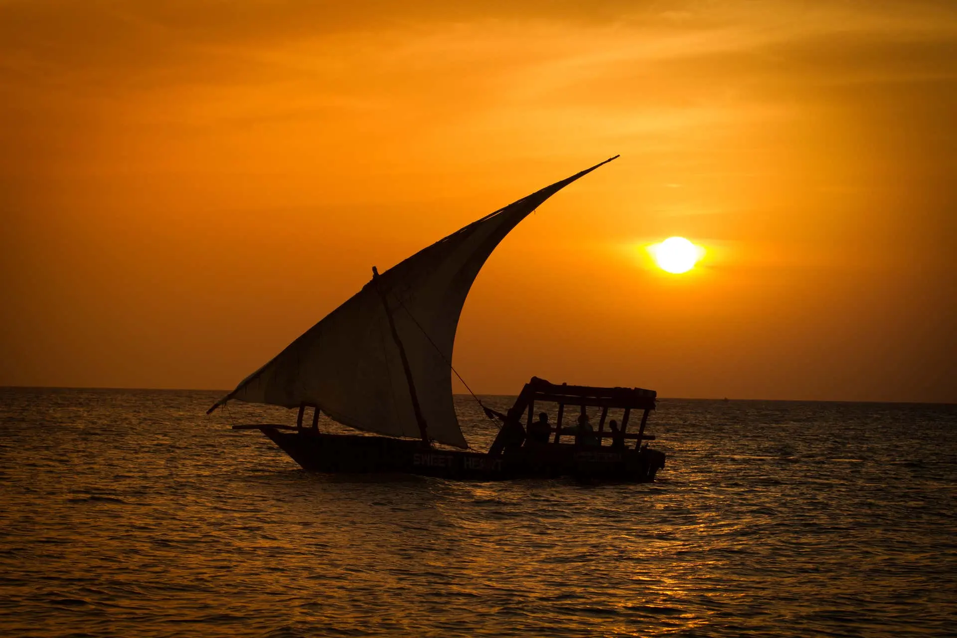 Traditional dhow sailing across calm water at sunset